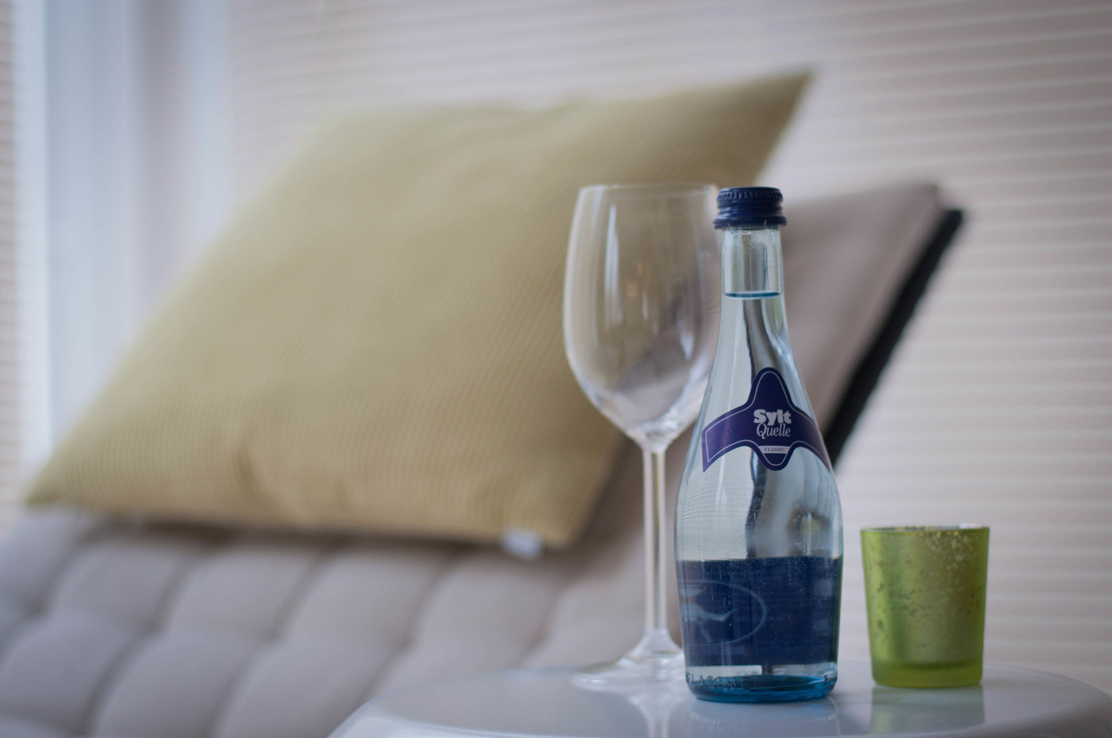 A bottle of water, a glass, and a green cup on a white table.