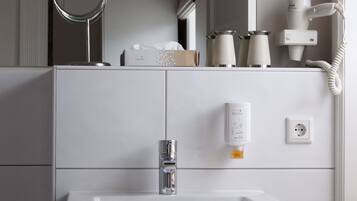 Un baño con lavamanos blanco, espejo y secador de pelo en la encimera.