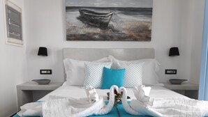 A hotel room with a bed, two nightstands, a painting of a boat on the wall, and a blue pillow. - Santoxenia Luxury Villa (Santorini)
