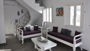 A modern living room with a white staircase, two white sofas with purple cushions, a white coffee table, and a decorative white chandelier. - Santoxenia Luxury Villa (Santorini)