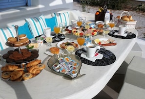 Un buffet de petit-déjeuner proposant une variété de viennoiseries, de fruits et de boissons, le tout disposé sur une table à l’extérieur.