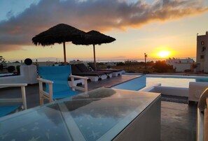 Un espace piscine aménagé sur le toit, avec des chaises longues et des parasols, offrant une vue sur le coucher de soleil sur la mer.