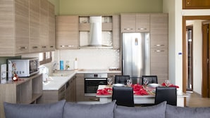 A modern kitchen with wooden cabinets, a stainless steel refrigerator, and a dining area with a table set for two. - Villa Saint George (Rethymno)