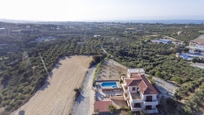 An aerial view of a property with a swimming pool, terraced fields, and a large building with a red roof. - Villa Saint George (Rethymno)
