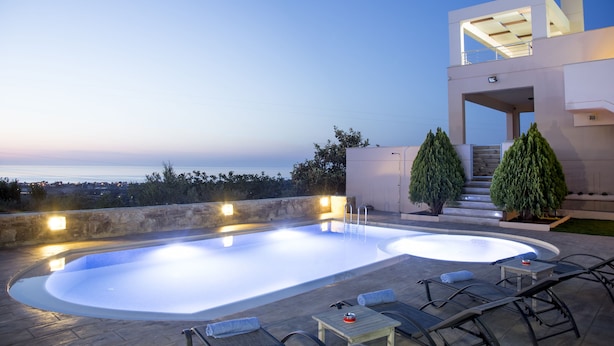 A modern outdoor swimming pool with lounge chairs and a view of the sea. - Villa Saint George (Rethymno)