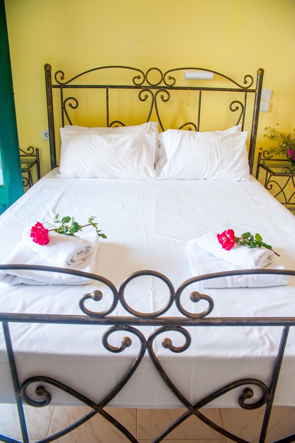 A neatly made bed with white linens and two red roses on folded towels, set against a yellow wall.
