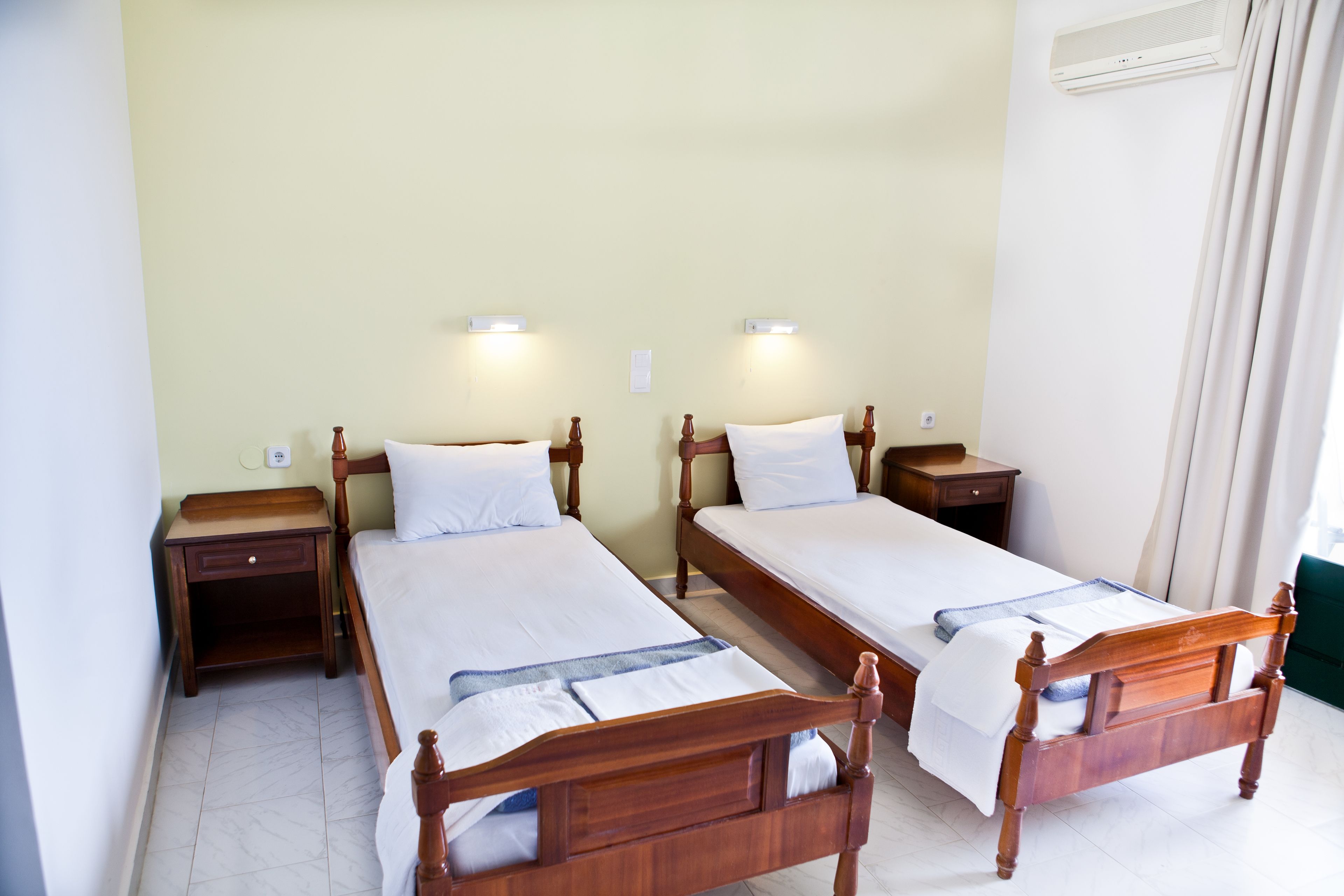 A hotel room with two wooden beds, nightstands, and wall-mounted lights.
