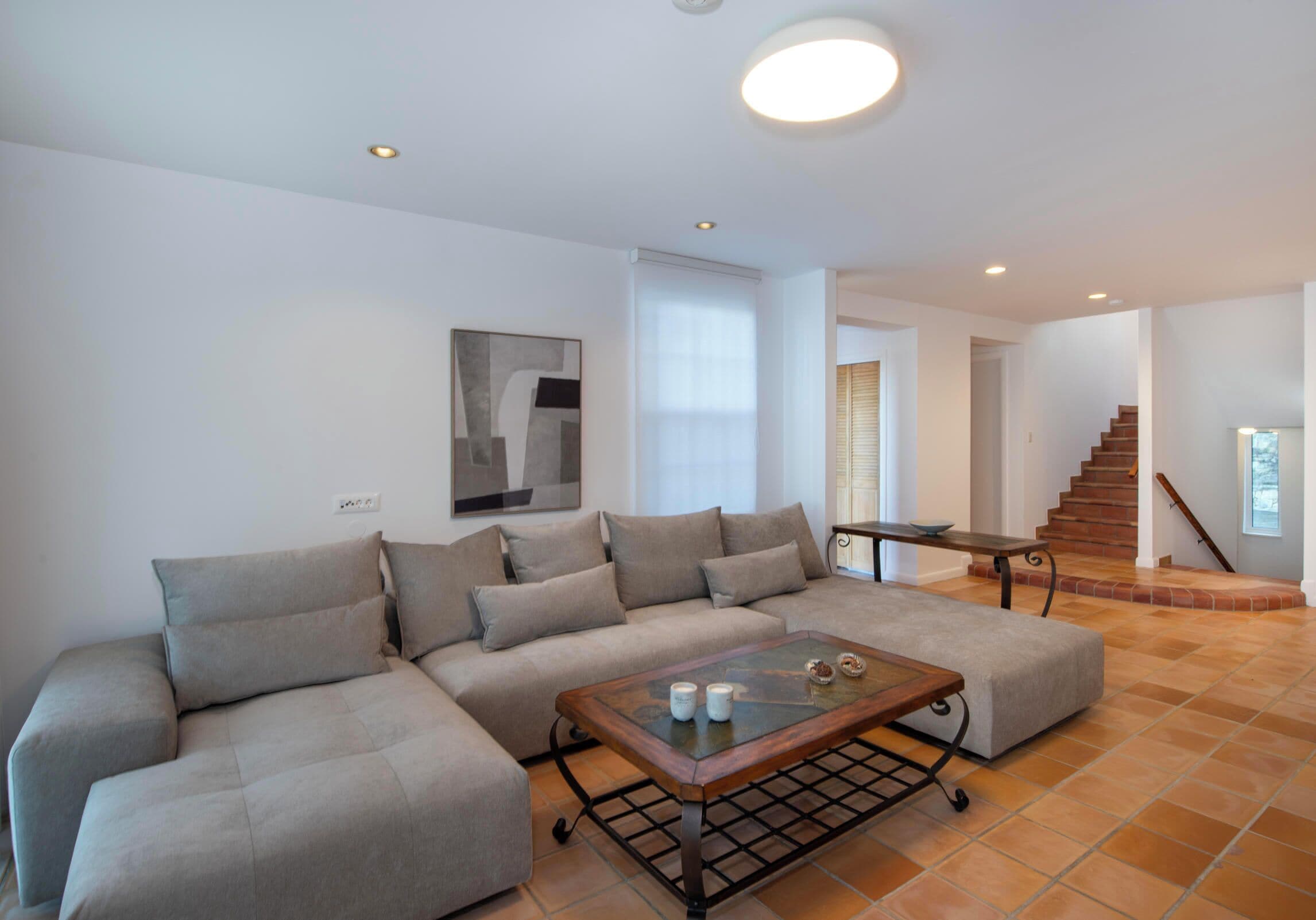 A modern living room with a sectional sofa, a glass coffee table, and a staircase leading to an upper level.
