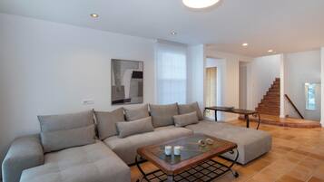 A modern living room with a sectional sofa, a glass coffee table, and a staircase leading to an upper level.