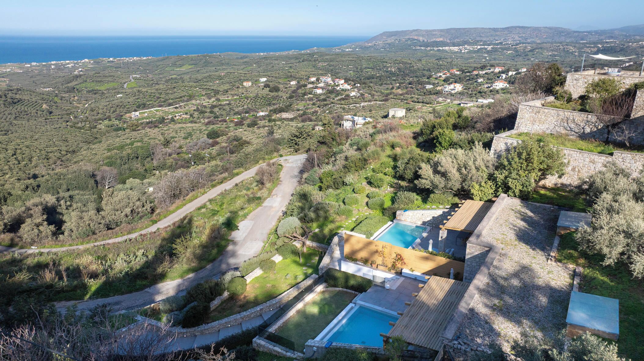 A villa with a swimming pool, stone walls, and a view of the sea and surrounding landscape.