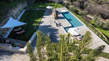 Vista aérea de un área de piscina privada con sillones de descanso, una gran formación rocosa y vegetación circundante.