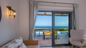 A room with a bed, a table with two glasses of red wine, a chair, and a view of the sea through a glass door. - Thea Villas Complex (Apokoronas)