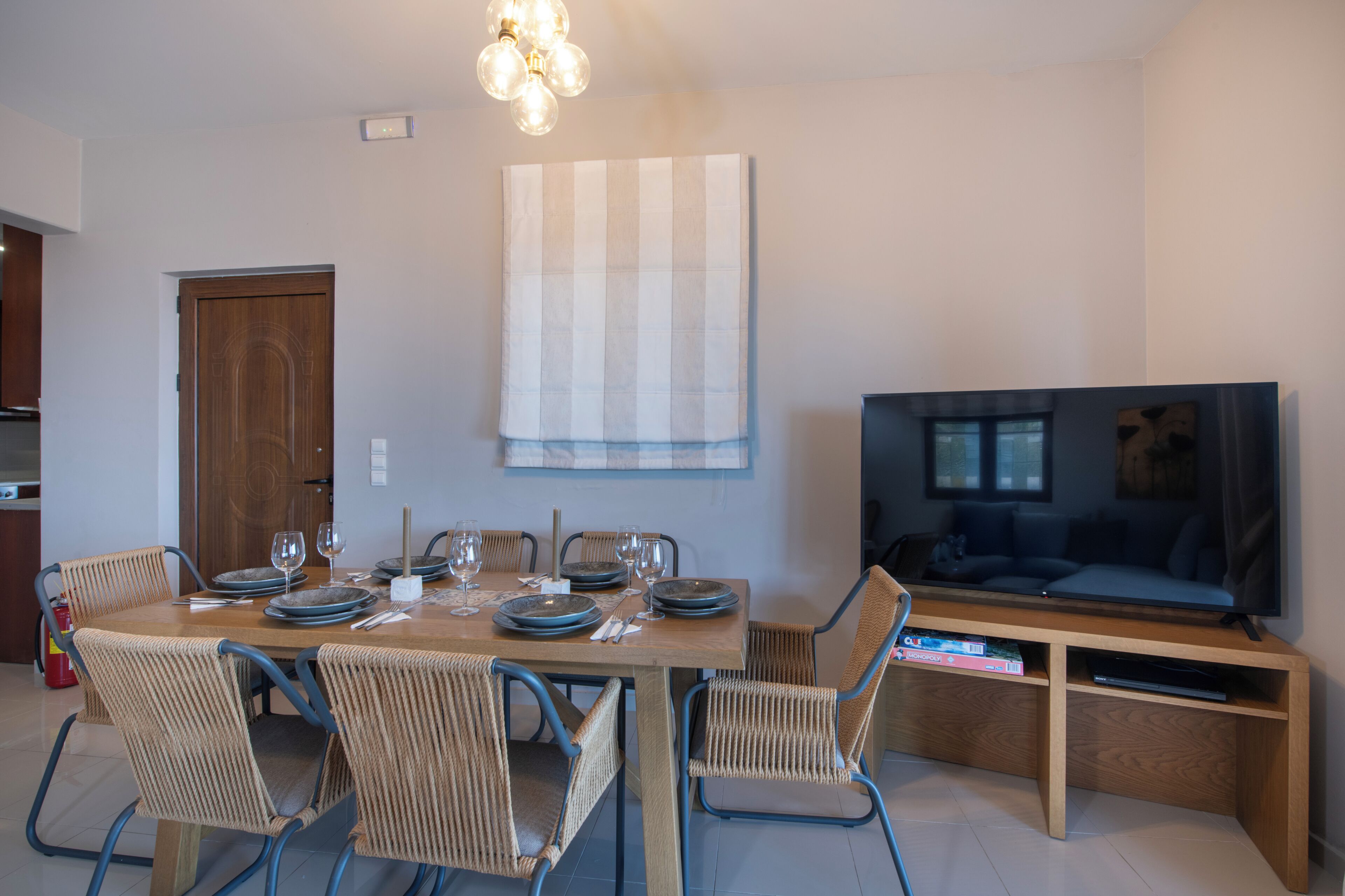 Un comedor con una mesa de madera, sillas de mimbre y un televisor sobre un mueble de madera.