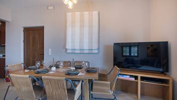 A dining area with a wooden table, wicker chairs, and a television on a wooden stand.