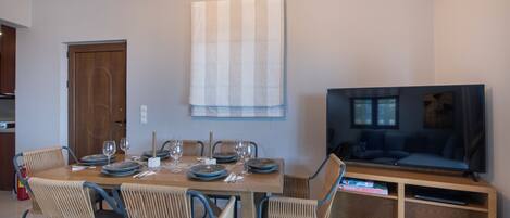 Un comedor con una mesa de madera, sillas de mimbre y un televisor sobre un mueble de madera.