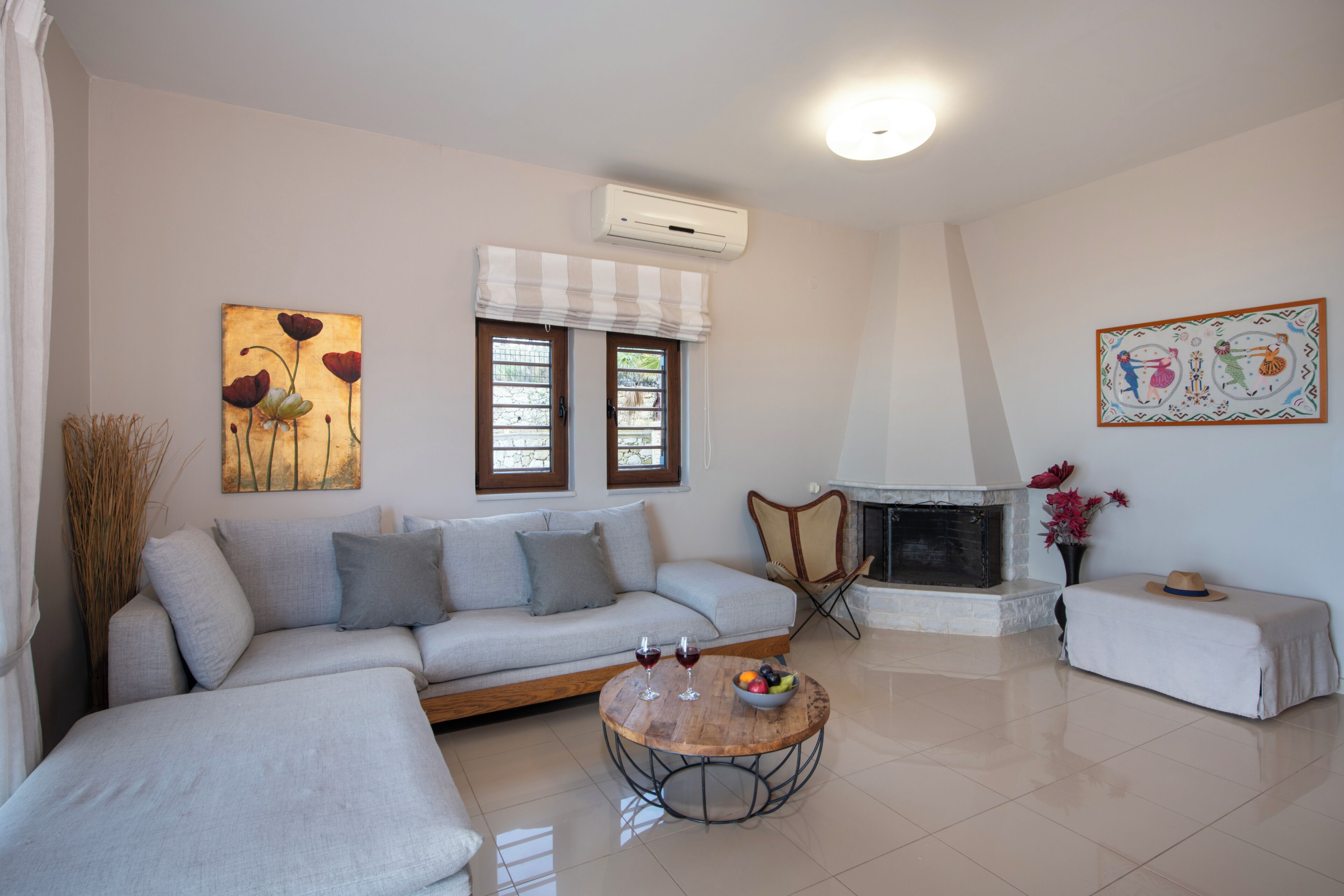 A living room with a sofa, a round coffee table with a fruit bowl, a fireplace, and artwork on the walls.