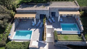 A two-story stone building with a pool, outdoor seating, and a staircase. - Thea Villas Complex (Apokoronas)