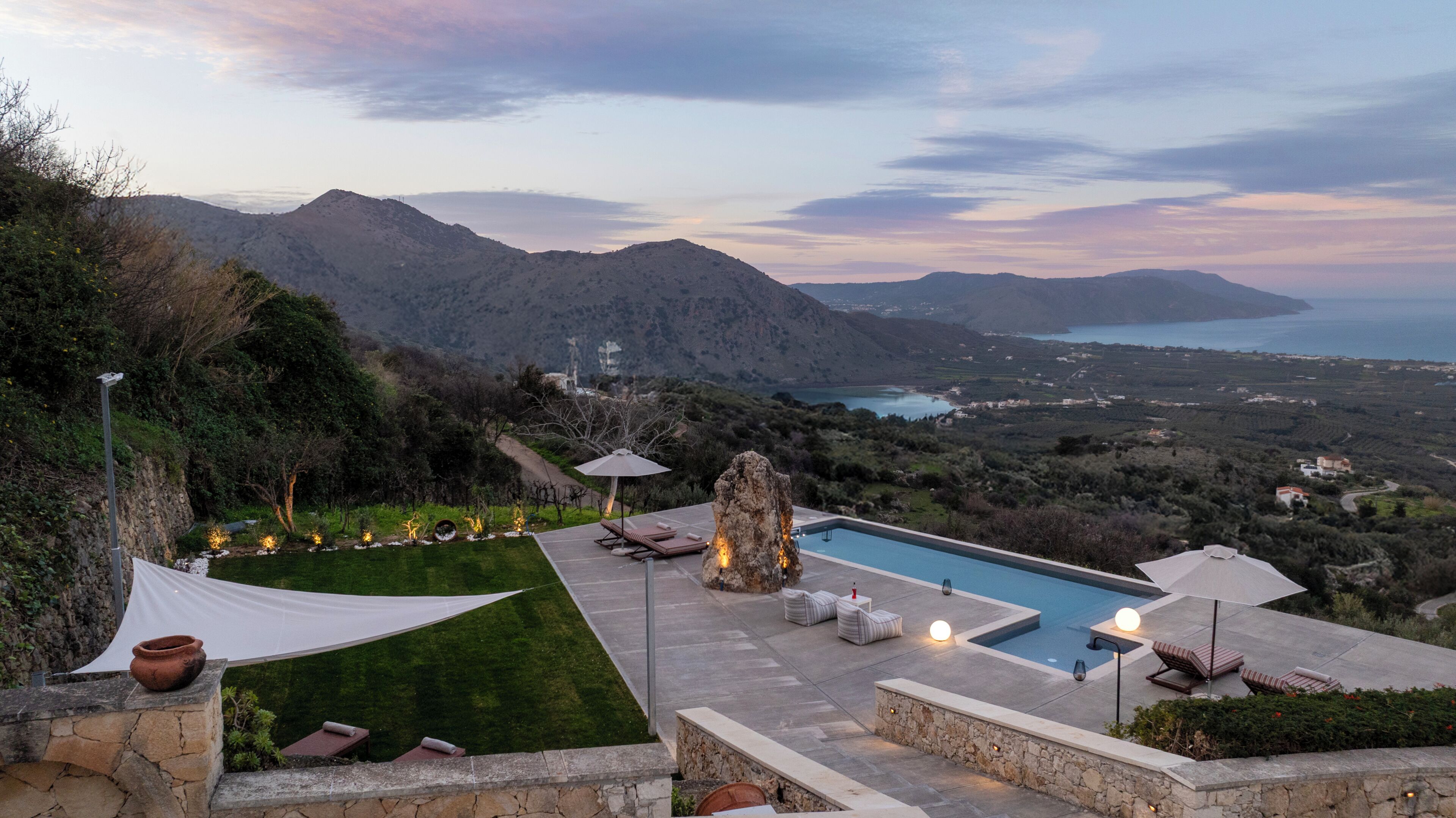 A pool area with a view of the sea and mountains, outdoor seating, and a white canopy.