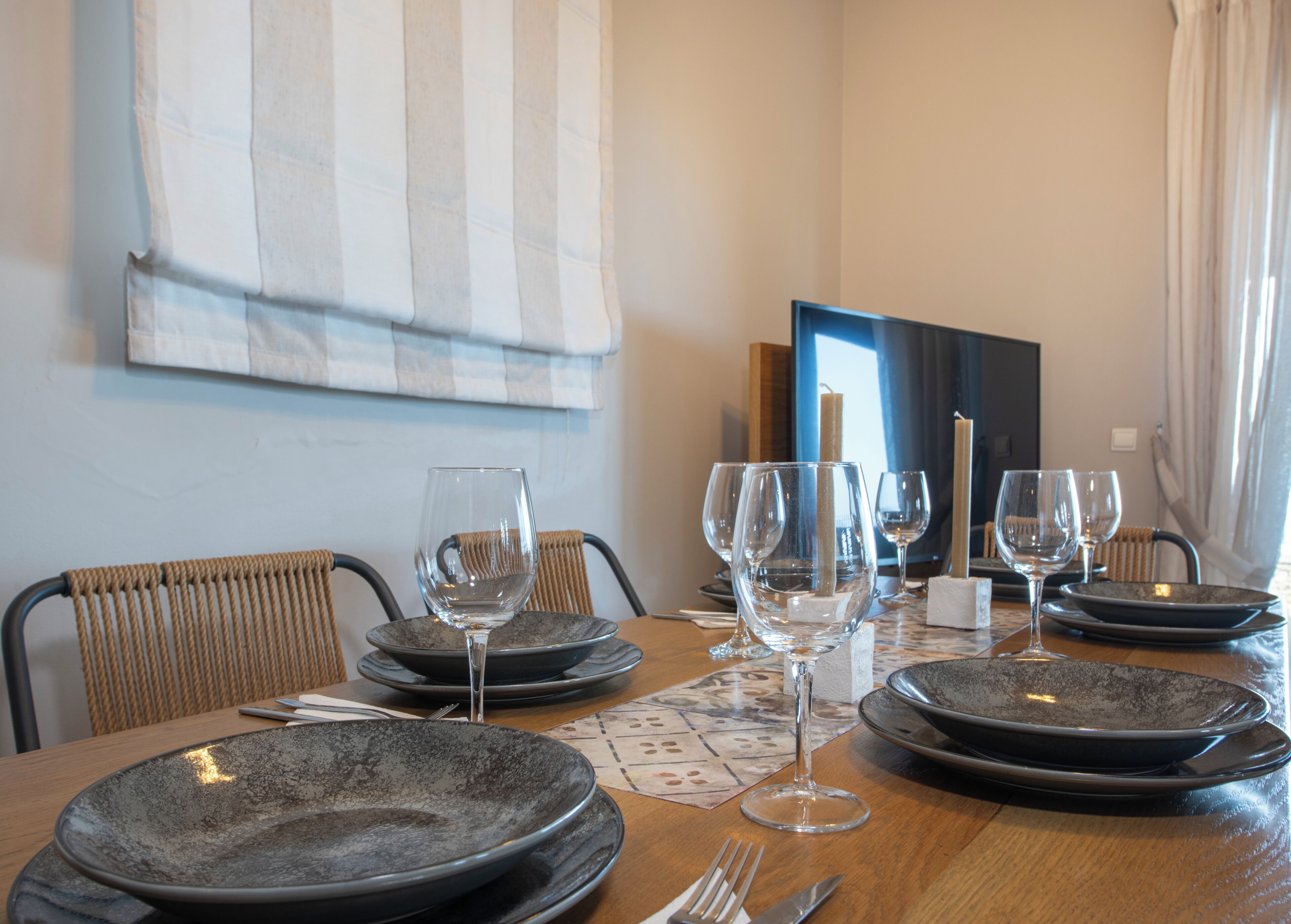 Une table à manger dressée avec des assiettes, des verres et des couverts, avec une chaise et une fenêtre en arrière-plan.
