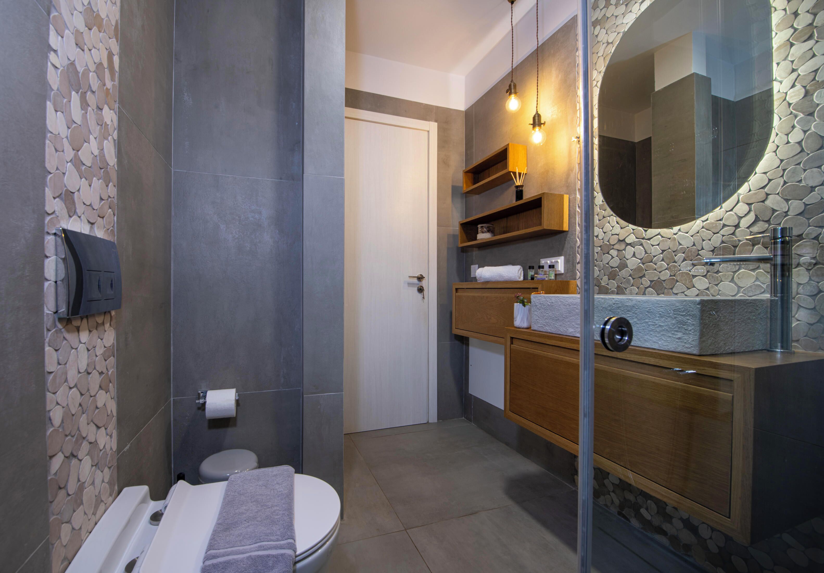 A bathroom with a toilet, a sink with a stone countertop, a mirror with a stone frame, and a towel rack.