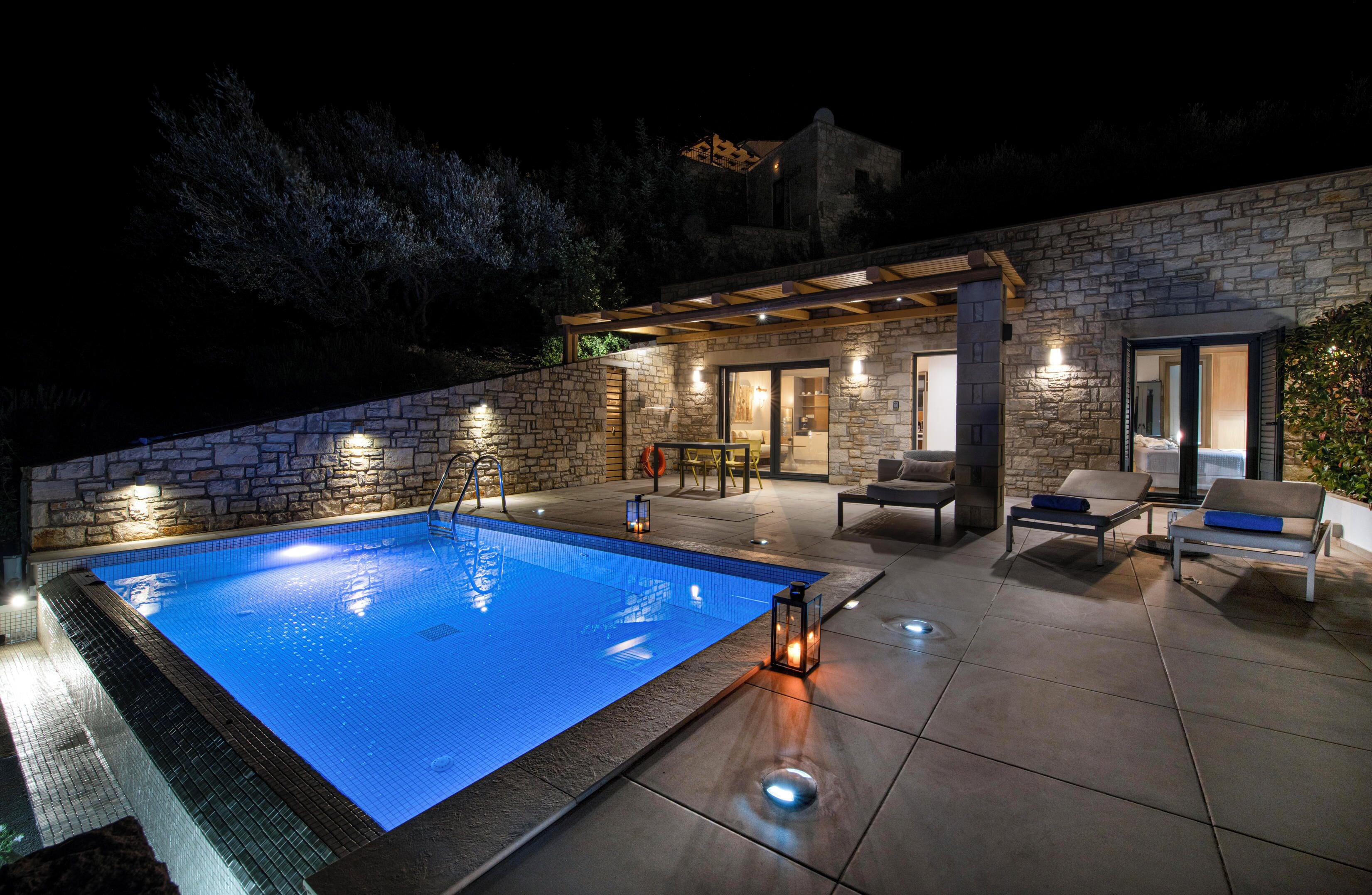 Piscina con muro de piedra, mobiliario exterior y una pérgola.