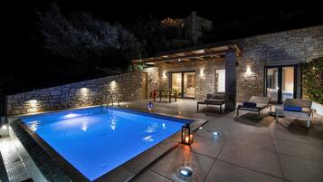 Piscina con muro de piedra, mobiliario exterior y una pérgola.