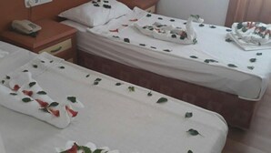 Une chambre d’hôtel avec deux lits simples, chacun recouvert d’une courtepointe blanche et agrémenté de pétales de rose. On y trouve une tête de lit en bois, une table de chevet avec un téléphone et une fenêtre avec des rideaux.