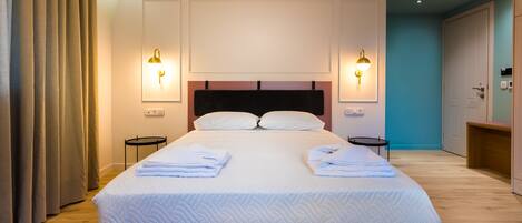 A neatly made bed with white linens and pillows, two bedside tables, and wall-mounted lighting.