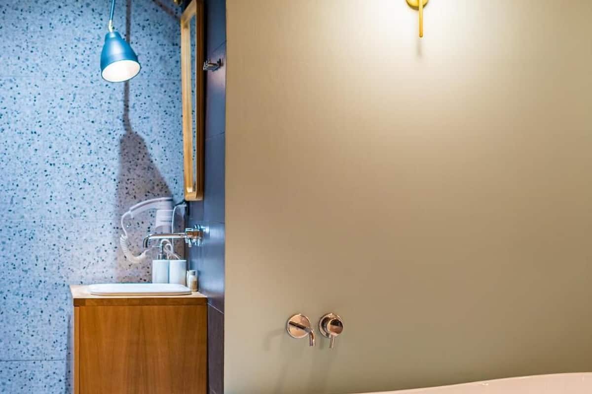 Un baño moderno con una bañera independiente, un tocador de madera, una lámpara colgante azul y un accesorio de luz en la pared.