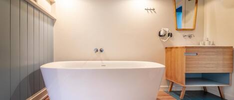 A modern bathroom with a freestanding bathtub, a wooden vanity, and a mirror.