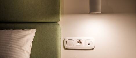 A bedroom with a bed, bedside table, and a wall socket.