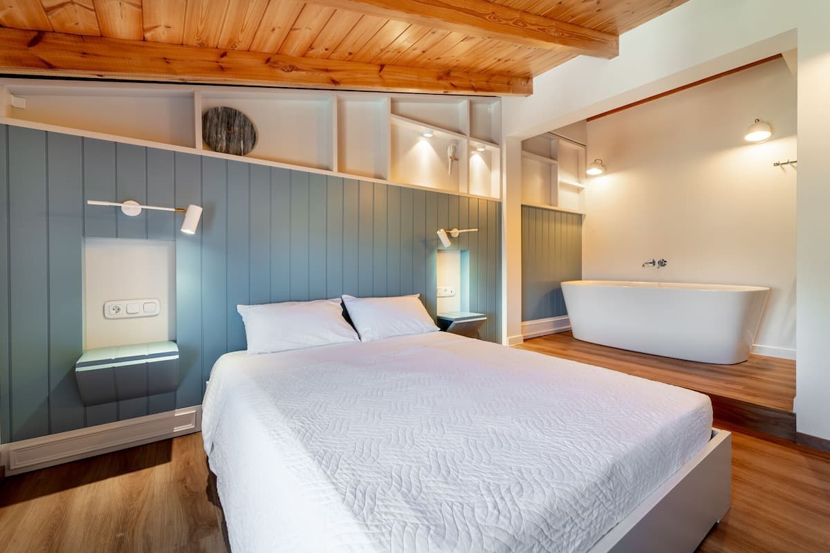 Un dormitorio moderno con una cama grande, un banco empotrado, un tocador con espejo y una bañera independiente.