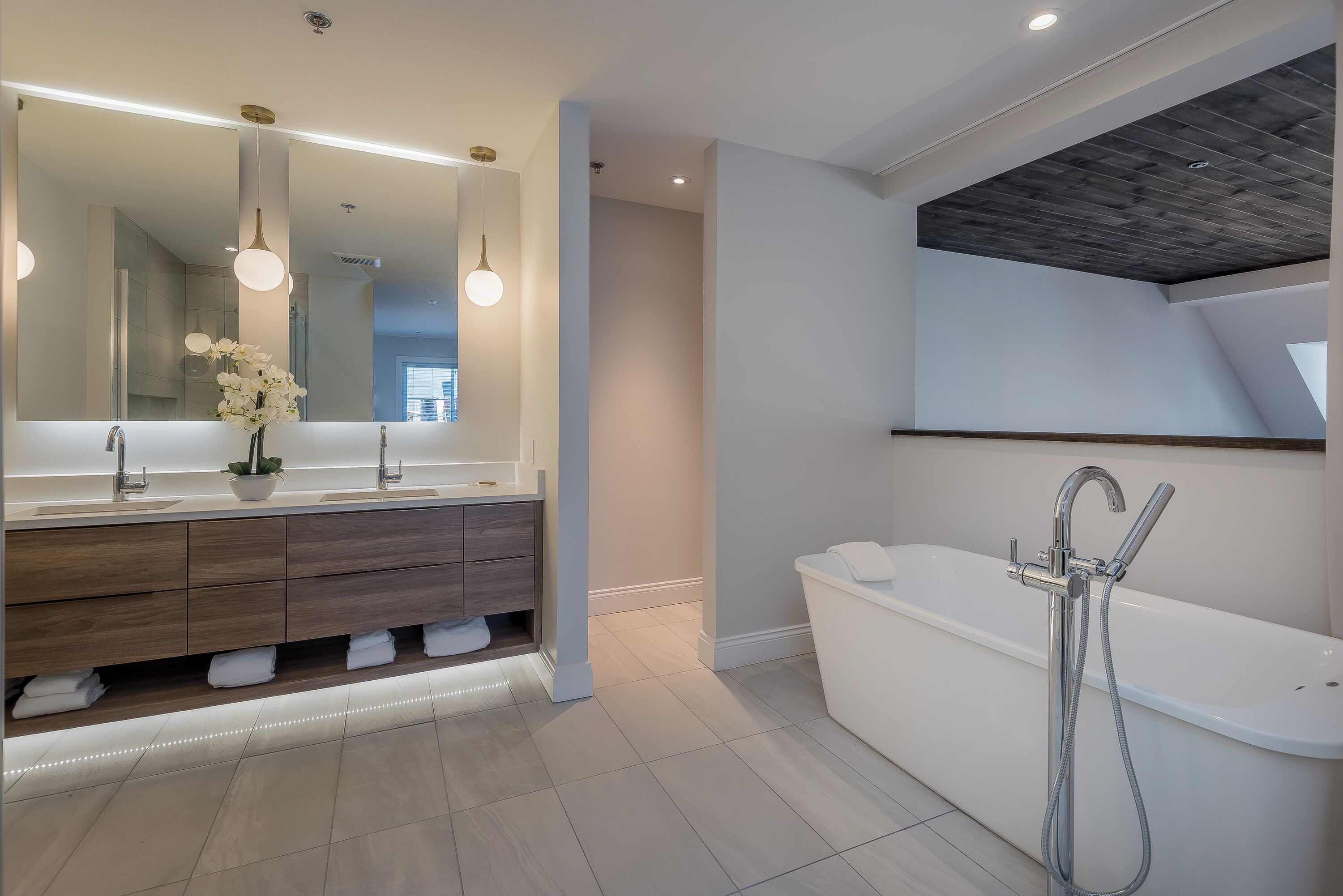 Un bagno moderno con un ampio specchio, doppio lavabo, mobile contenitore a incasso, vasca freestanding e illuminazione a incasso.