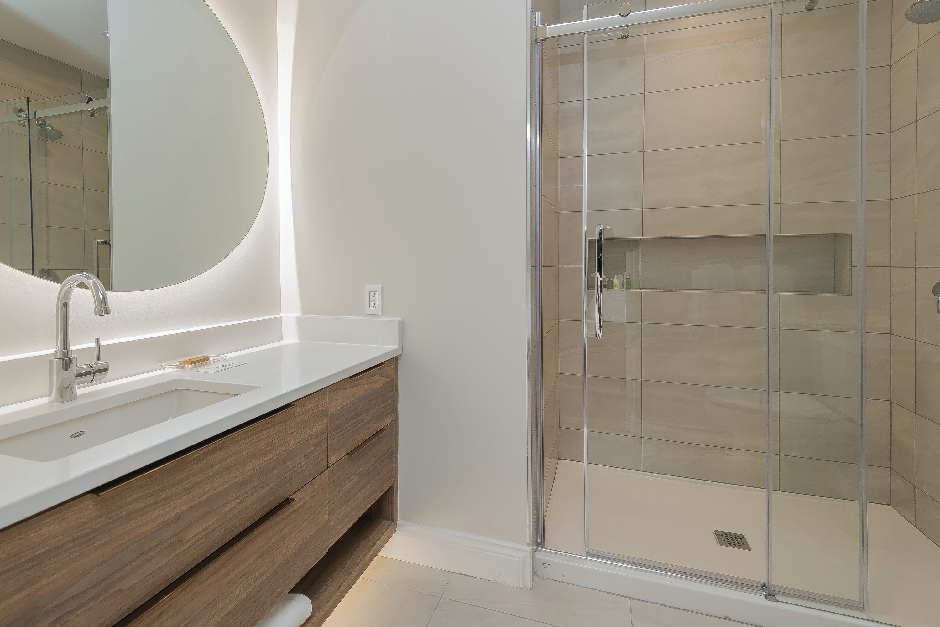 A modern bathroom with a glass shower enclosure, a large mirror, and a wooden vanity.