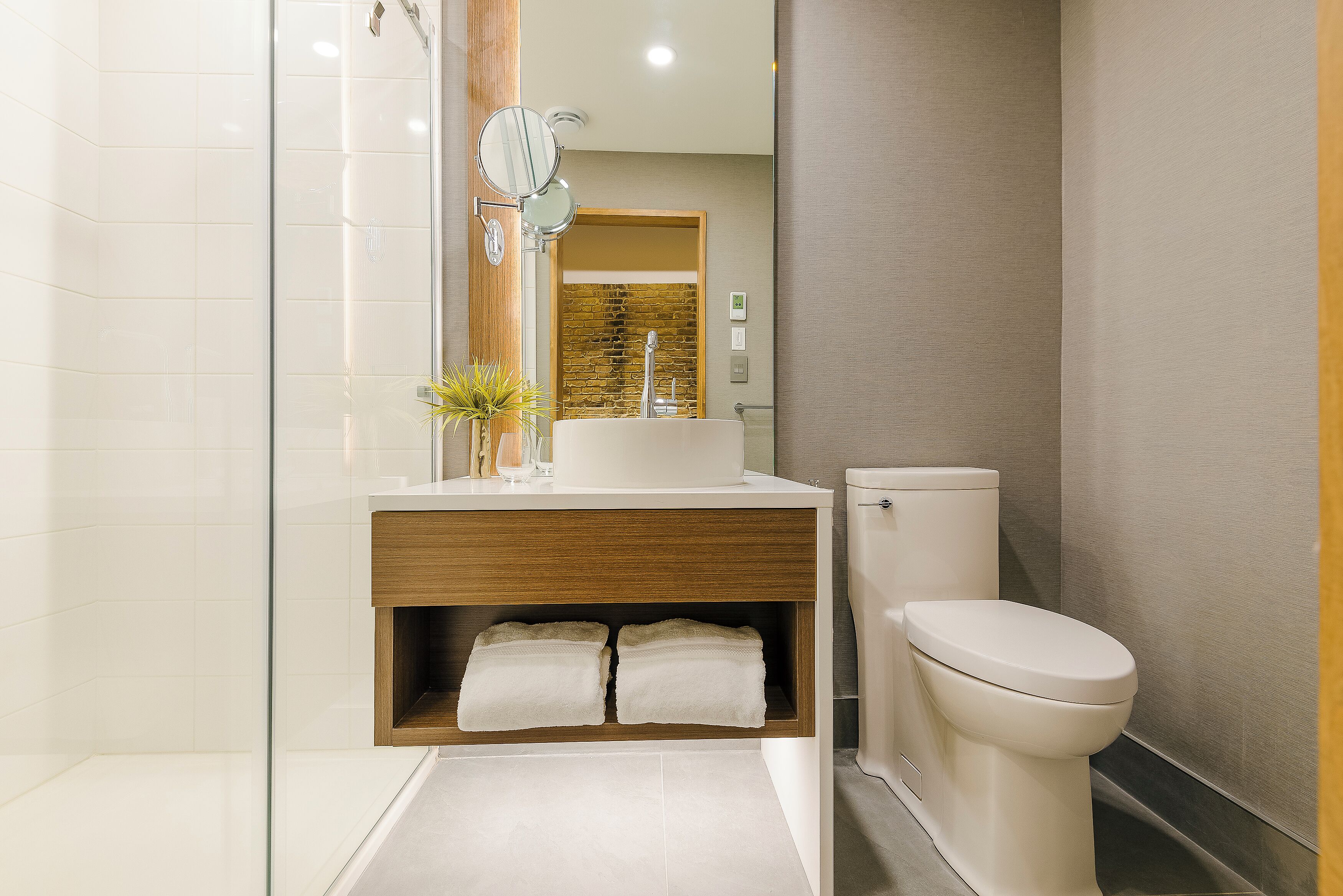 Un bany modern amb una cabina de dutxa de vidre, un moble de bany de fusta amb un lavabo i un vàter.