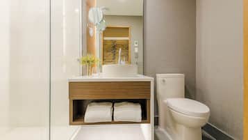 Un bany modern amb una cabina de dutxa de vidre, un moble de bany de fusta amb un lavabo i un vàter.