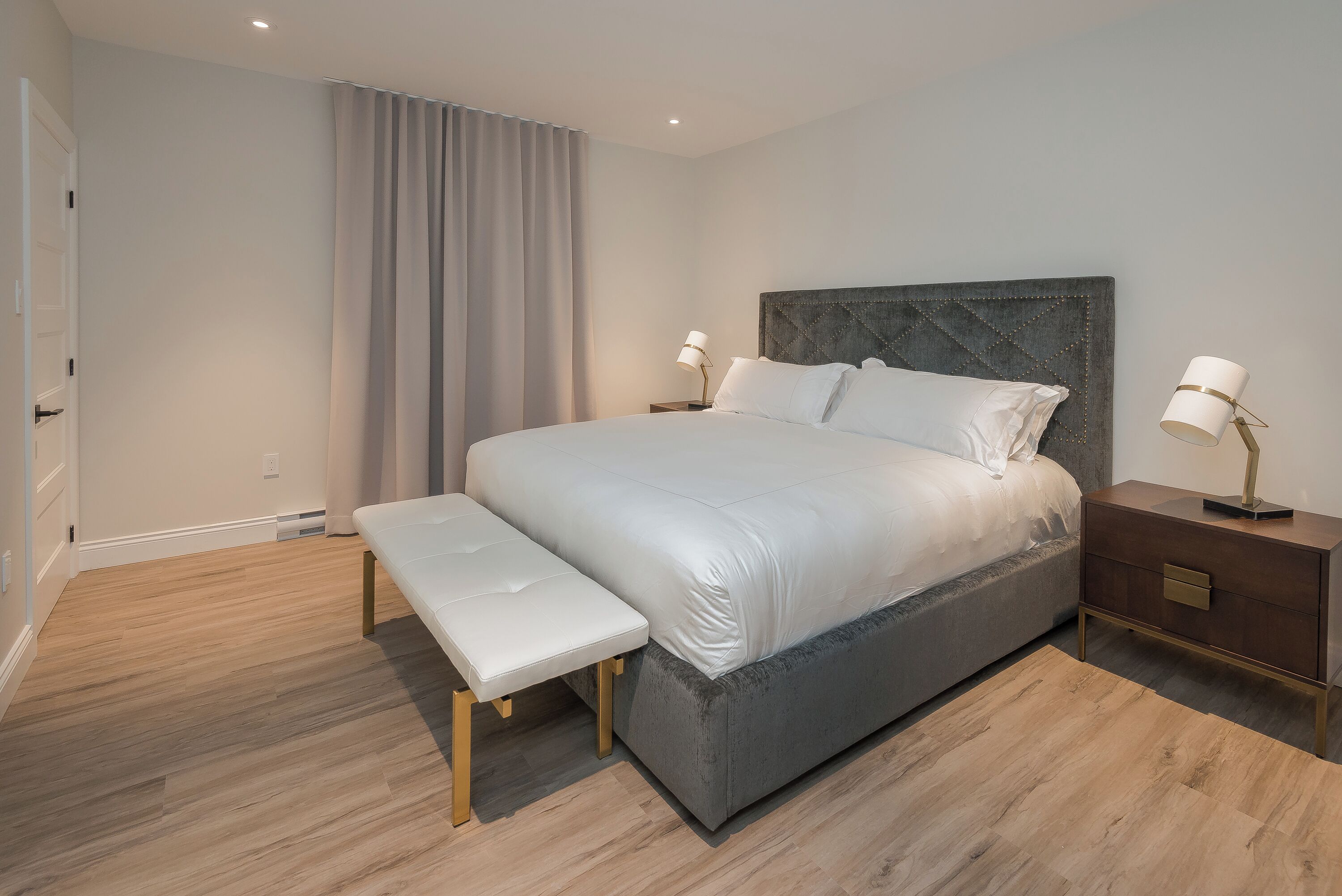 A modern bedroom with a large bed, a bench, two bedside tables, and a neutral color scheme.