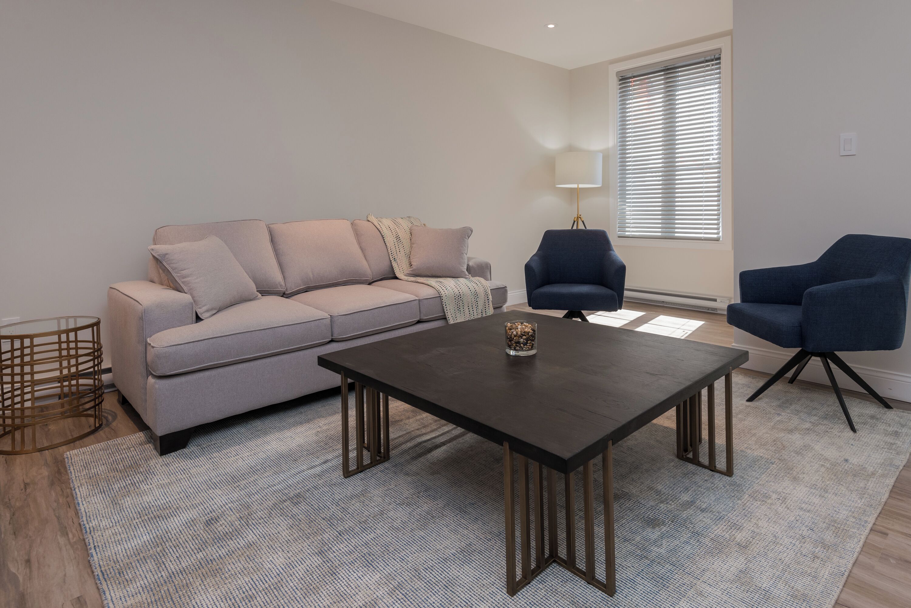 A modern living room with a grey sofa, a dark wooden coffee table, and two blue armchairs.