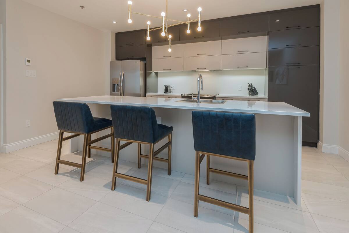 Una cocina moderna con una isla central, taburetes de bar y un refrigerador de acero inoxidable.