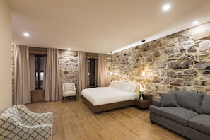 A bedroom with a stone wall, a bed, a grey sofa, and a patterned armchair. - La Maison Kent - Par Aneyro (Québec City)