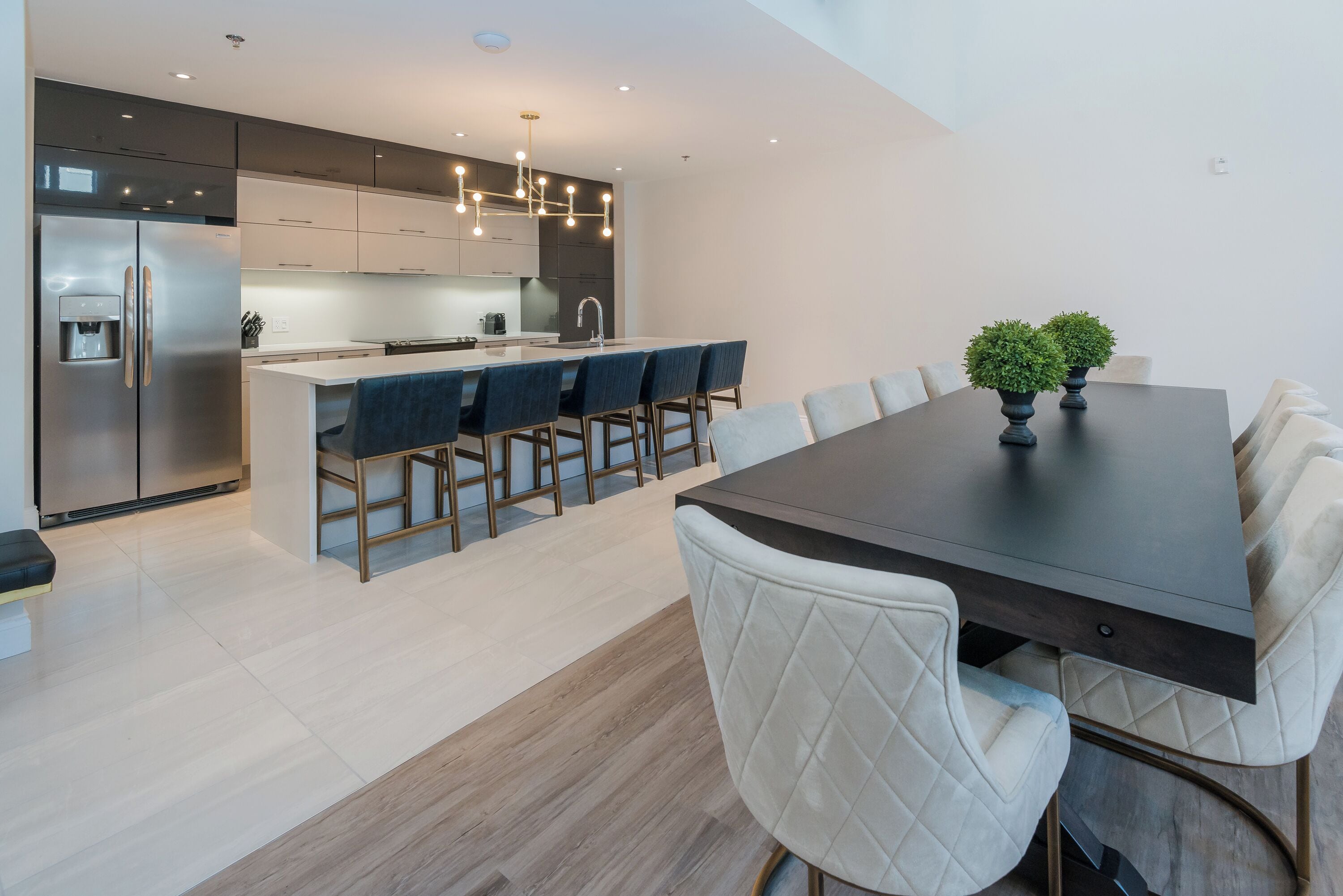 A modern kitchen with a central island, stainless steel appliances, and a dining area with a dark table and white chairs.