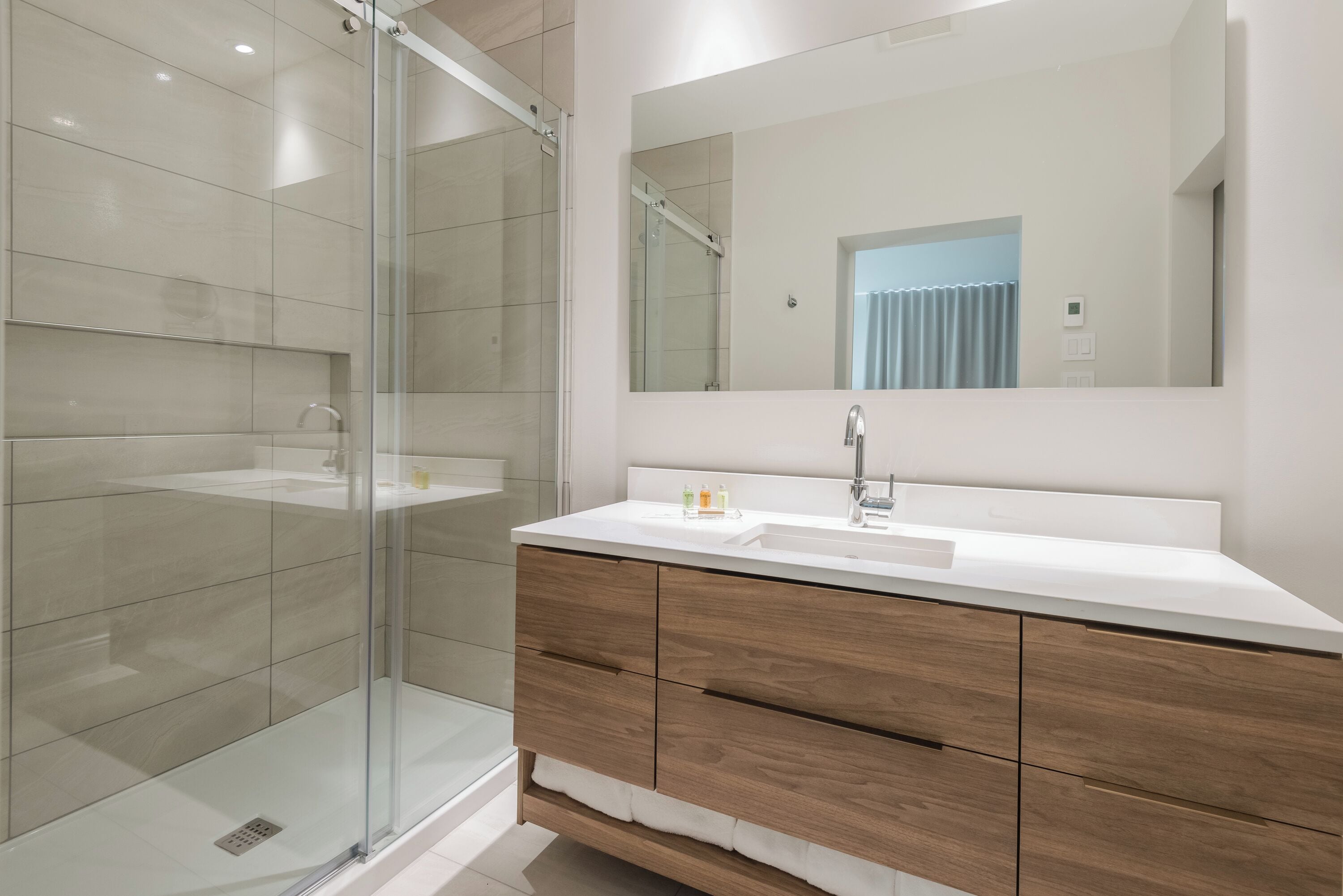 A modern bathroom with a glass shower enclosure, a white sink, and wooden cabinetry.