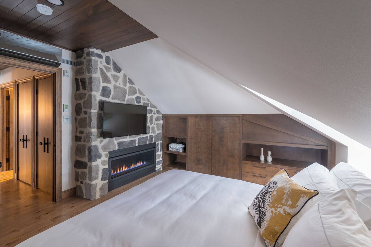Un dormitorio con chimenea de piedra, muebles de madera y televisor montado encima.
