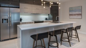 A modern kitchen with a large island, stainless steel appliances, and bar stools. - La Maison Kent - Par Aneyro (Québec City)