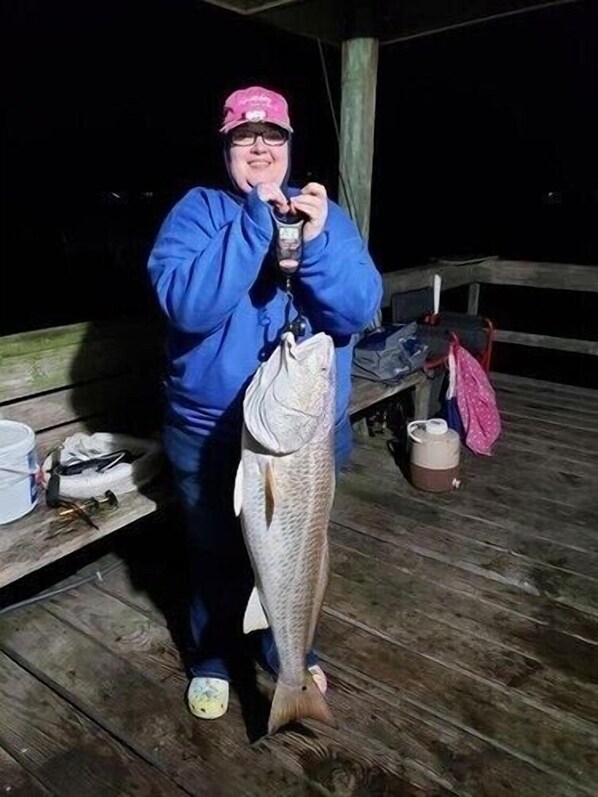 Una persona sosteniendo un pez en un muelle de madera de noche.
