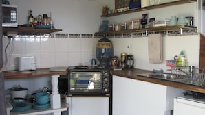 A compact kitchen with a built-in microwave, toaster, and coffee maker. Shelves hold various kitchen items and dishes.