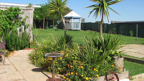 A garden with a birdbath, a gazebo, and a wheelbarrow.