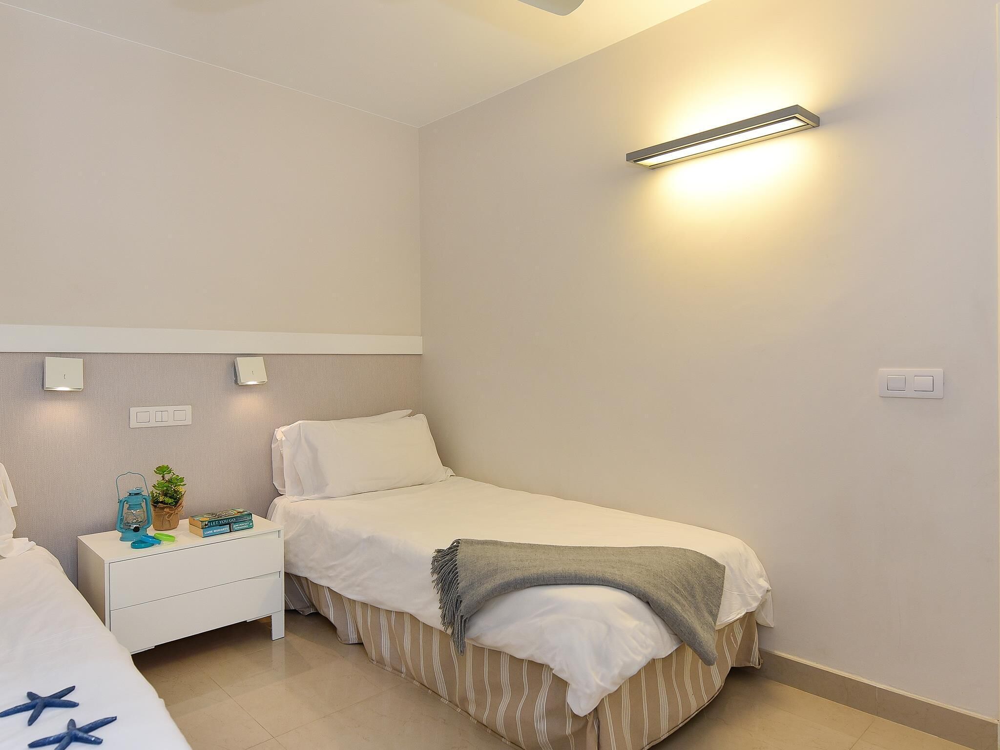 Een slaapkamer met een enkel bed, een nachtkastje met een lamp en een wandlamp.