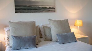Un letto rifatto con molti cuscini e un quadro incorniciato con vista sull'oceano.
