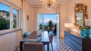 Zona pranzo con lampadario, tavolo e sedie, vista sul mare e uno specchio decorativo.